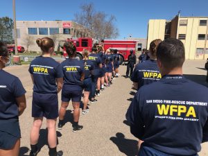 Picture of people in blue uniforms lined up in front of red fire engine