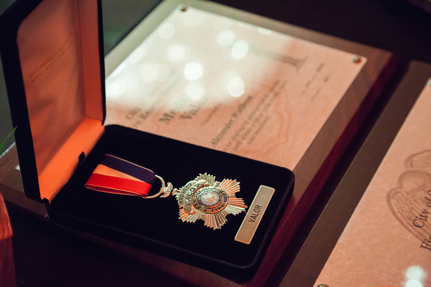 Picture of a medal of valor pin displayed on black velvet in a jewelry box sitting next to an award plaque.